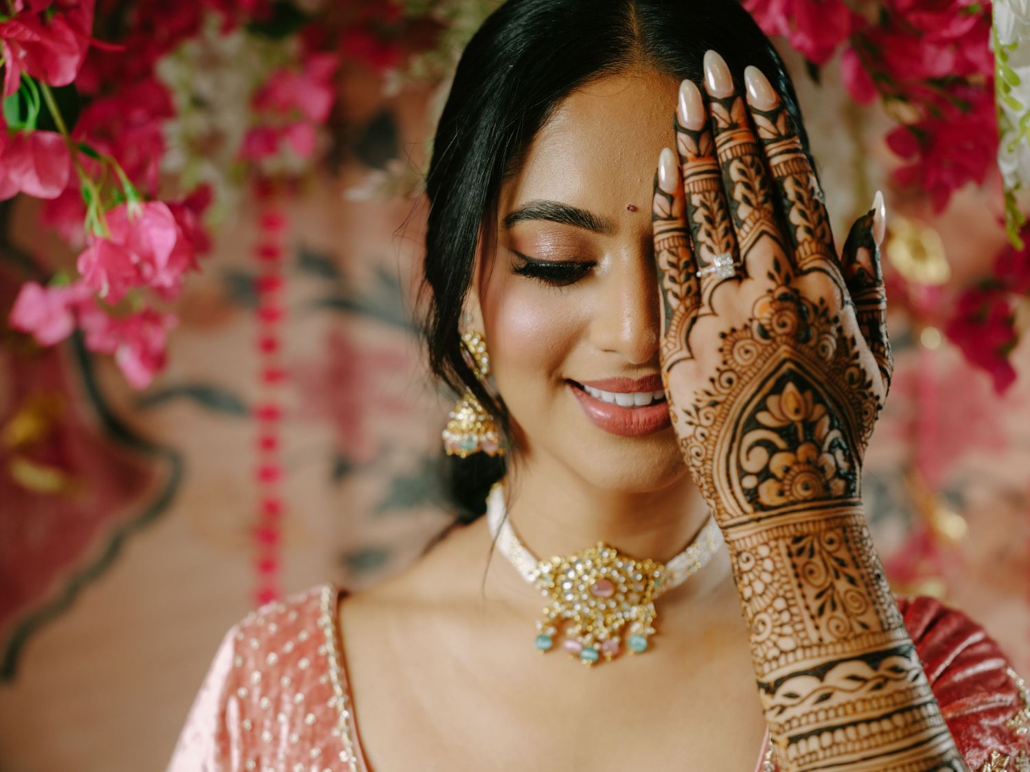 Close-up of traditional bridal mehndi design on hand with pink floral background.