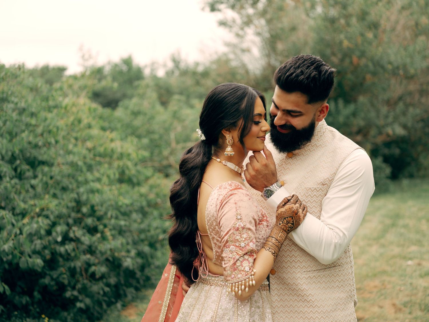 A couple in traditional South Asian attire embrace outdoors in a romantic garden setting.