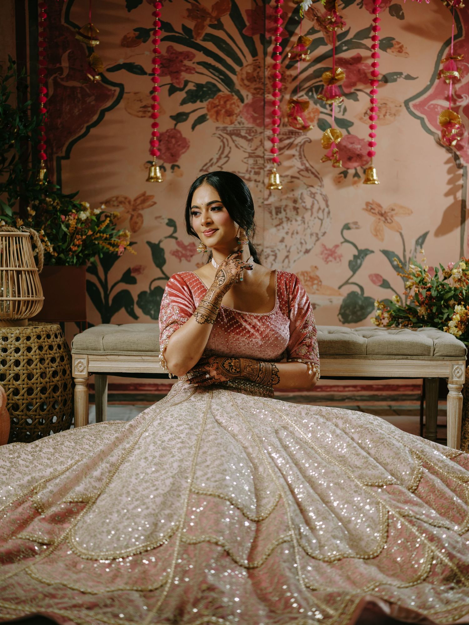 Traditional bridal attire featuring a pink blouse and white sequined lehenga against floral wallpaper with decorative elements.