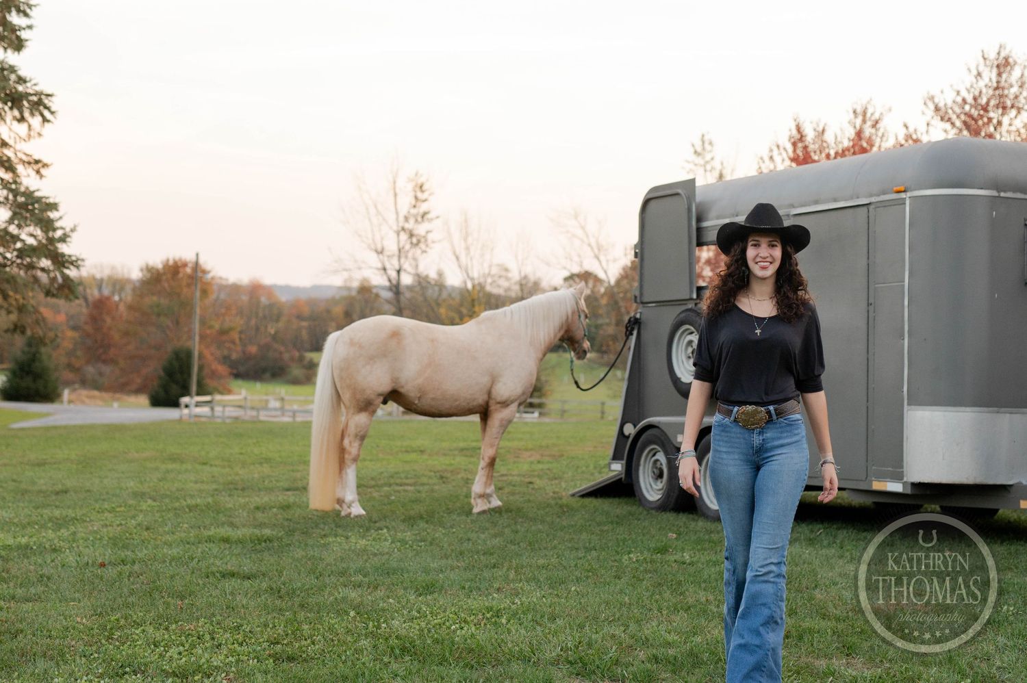 Natural outdoor photo featuring a white horse and silver trailer in a peaceful country setting.