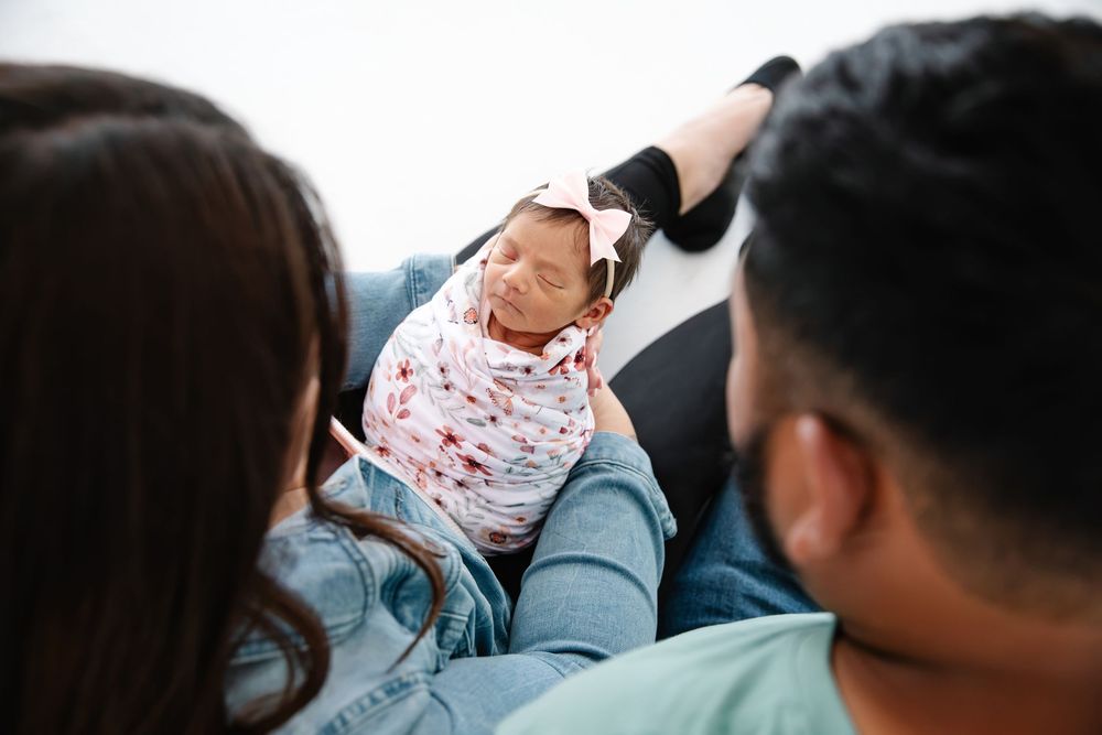 New parents lovingly gaze at their swaddled newborn baby wrapped in a pink floral blanket.