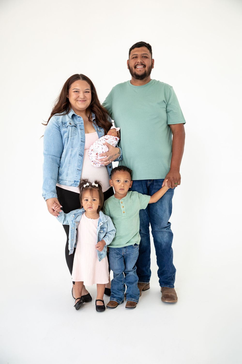 Happy family of four with newborn baby posing together in a studio portrait against a white background.
