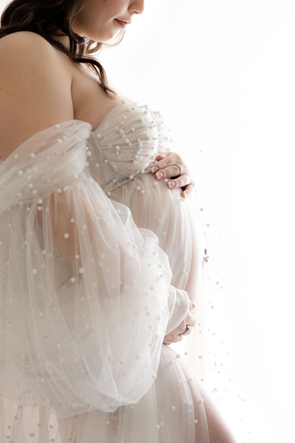 Ethereal white maternity gown with delicate pearls and flowing tulle captures an elegant pregnancy photo moment.