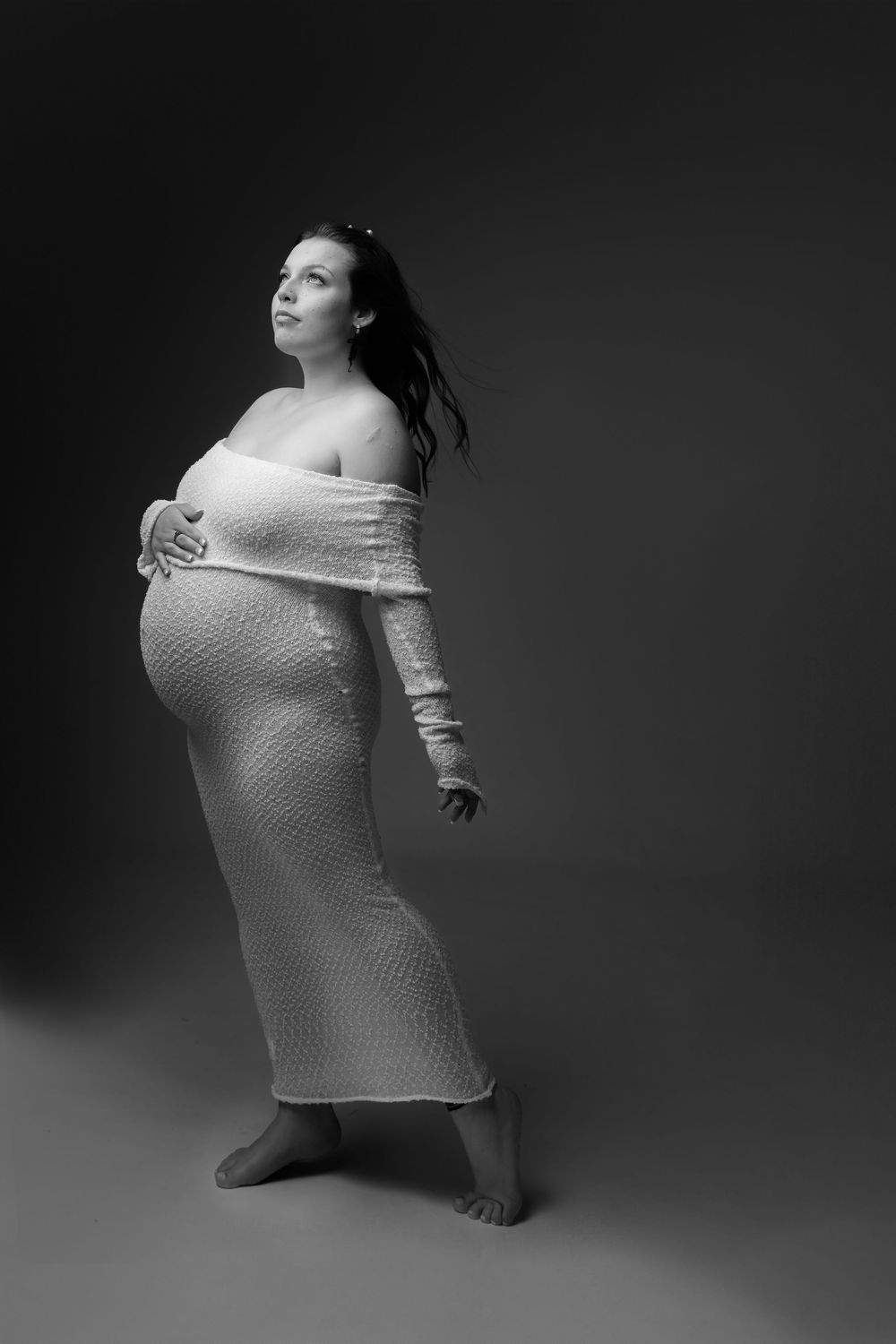 Black and white photo series showing artistic pregnancy portraits of a woman in soft fabric against dark backdrop.