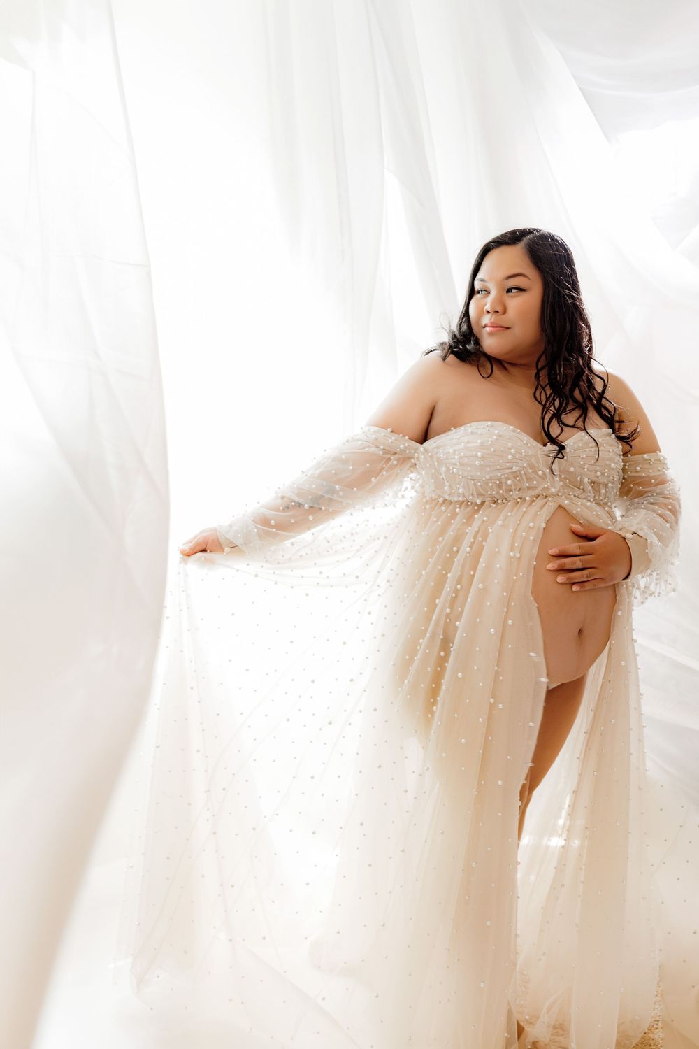 A dreamy boudoir portrait featuring soft white fabric and a flowing cream-colored dress in an ethereal setting.