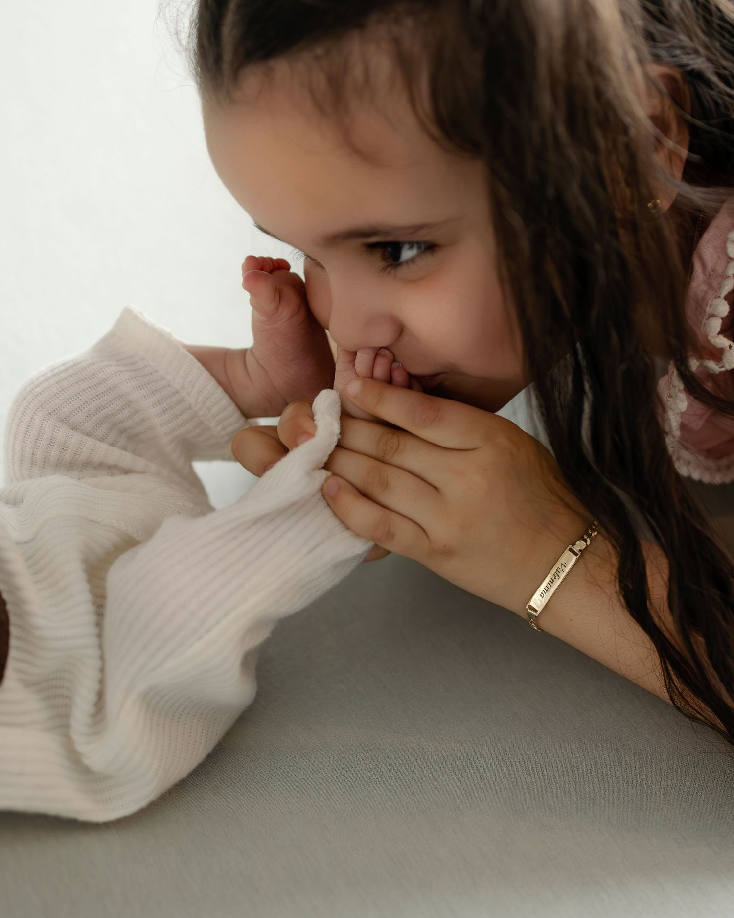 A small child covers their nose and mouth with hands while wearing a cream colored sweater.