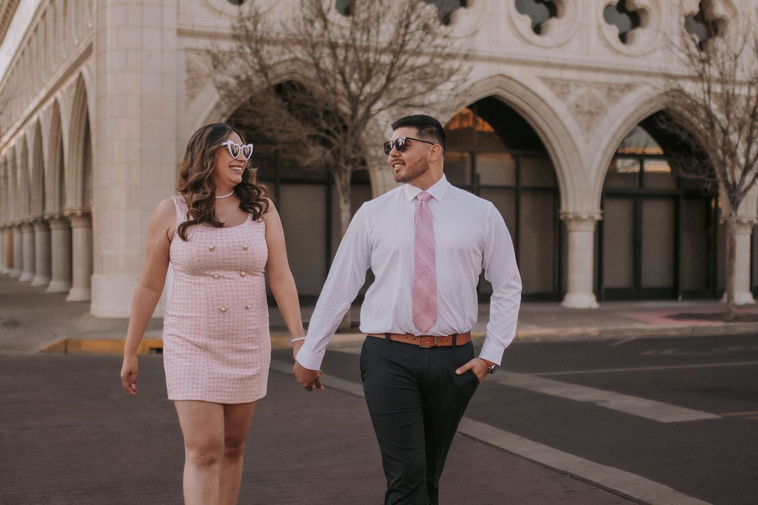 A couple walking and smiling outside a grand building w/ arched columns in Downtown Albuquerque New Mexico. Engagement session outfit ideas.