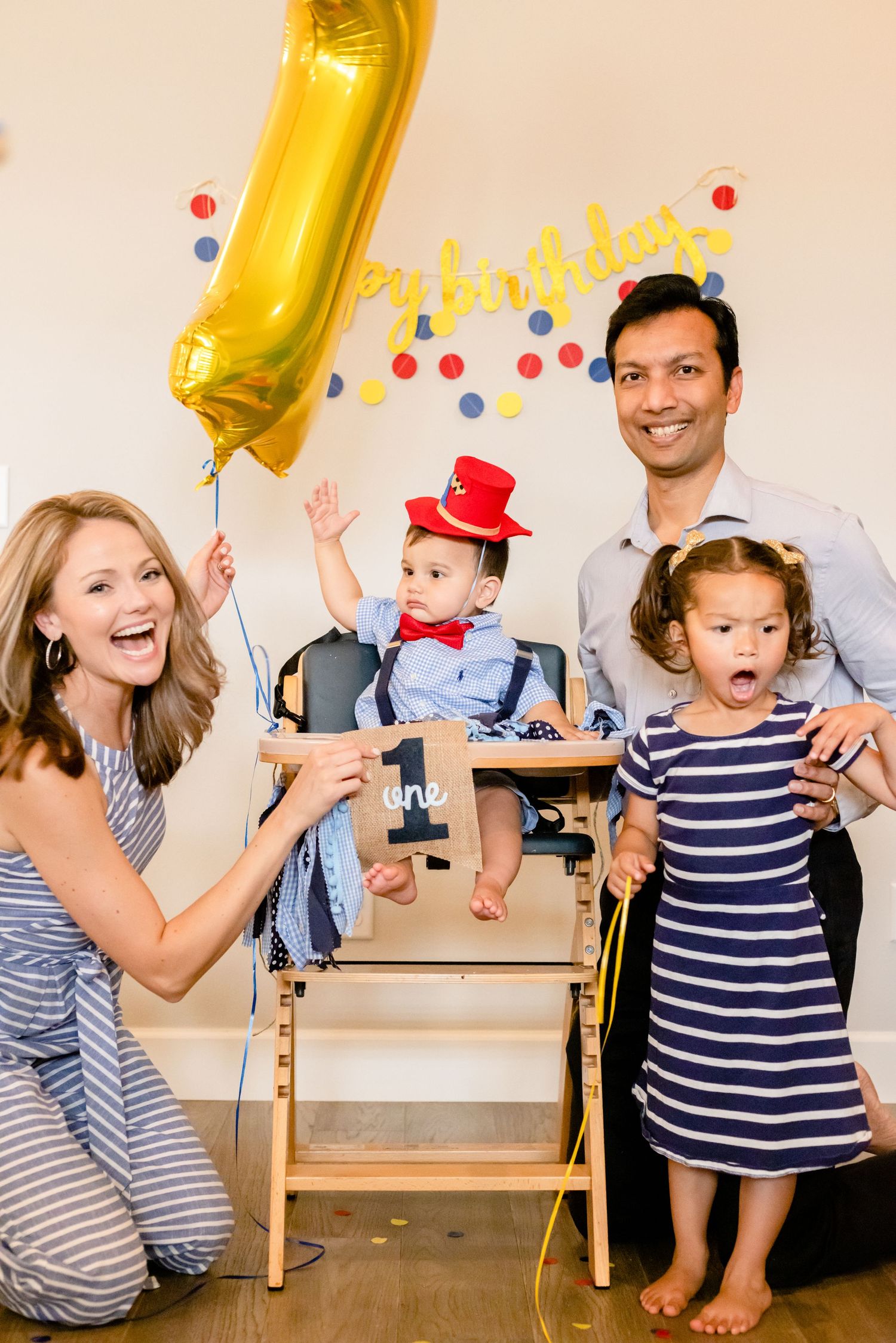 Family celebrates a first birthday party with gold balloon and festive decorations in their home.
