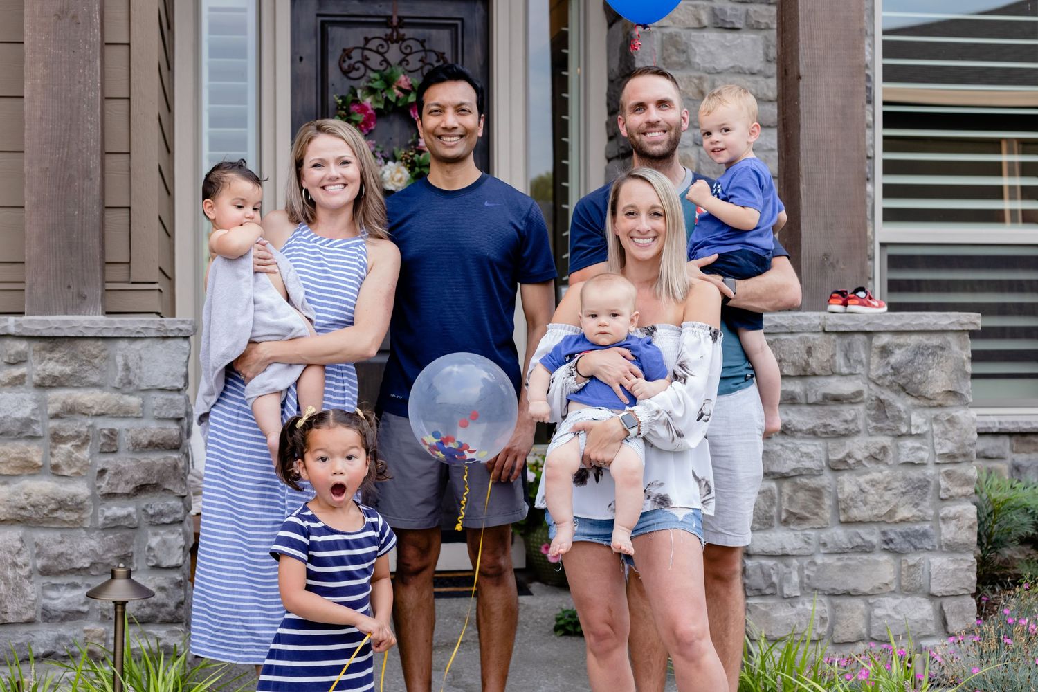 A group in coordinated blue and white outfits stands together on a stone porch holding balloons.