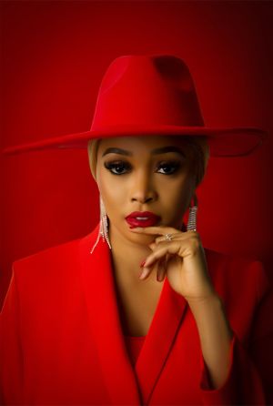 Striking fashion portrait featuring monochromatic red styling with hat, blazer and dramatic lighting against red backdrop.