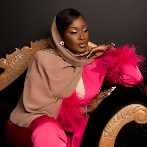 Stylish combination of beige hoodie and hot pink outfit with dramatic feathers against brown chaise lounge in studio portrait.
