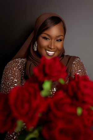 A glowing portrait with vibrant red roses and a sparkly brown dress against a dark background.