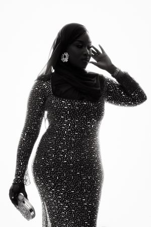 A silhouetted figure in a sparkling sequin evening gown poses elegantly with dramatic lighting and statement earrings.