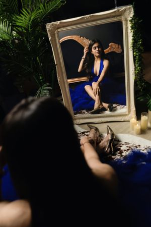 A decorative gold frame reflects an elegant image of someone wearing a royal blue dress against a dark background with palm leaves.