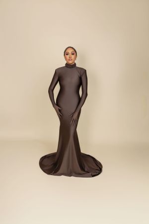 A form-fitting brown long sleeve gown with mermaid silhouette and train photographed against a beige background.
