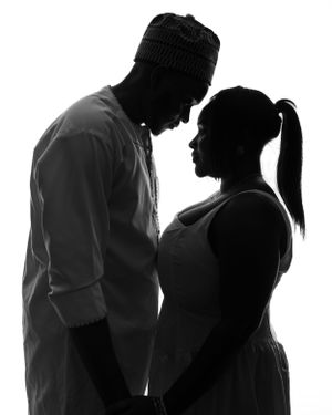 A silhouetted couple stands close together against white background, creating an intimate portrait in black and white.