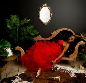 Dramatic portrait with flowing red tulle gown on vintage chaise lounge with faux cowhide rug and ornate mirror decor.