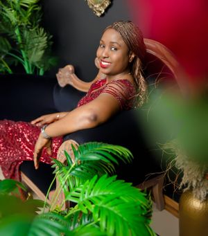 Elegant woman in sparkly red dress poses by tropical plants against dark wall with festive gold decor.