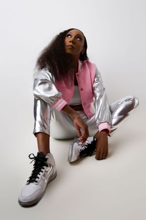 Stylish silver and pink varsity jacket worn with white pants and sneakers in modern fashion photo against white background.