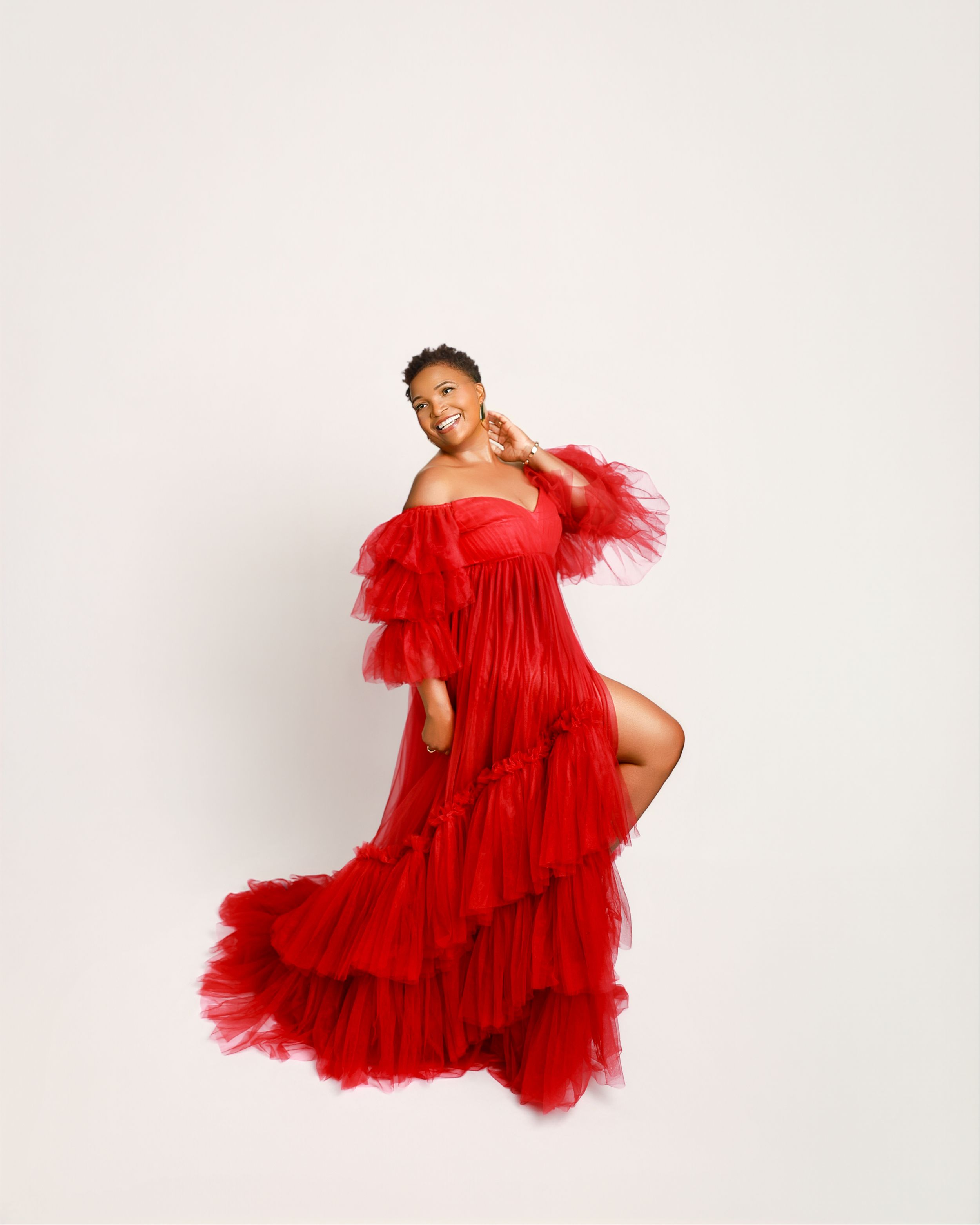 A fashion model in a voluminous red tulle gown poses gracefully against a white backdrop in a photo series.