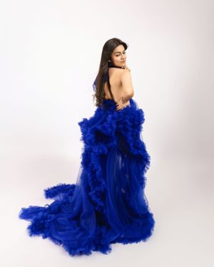 A flowing royal blue tulle gown with dramatic ruffles and a sweeping train photographed against a white backdrop.
