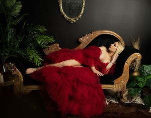 A dramatic boudoir photoshoot featuring a flowing red dress against a dark moody backdrop with natural foliage elements.