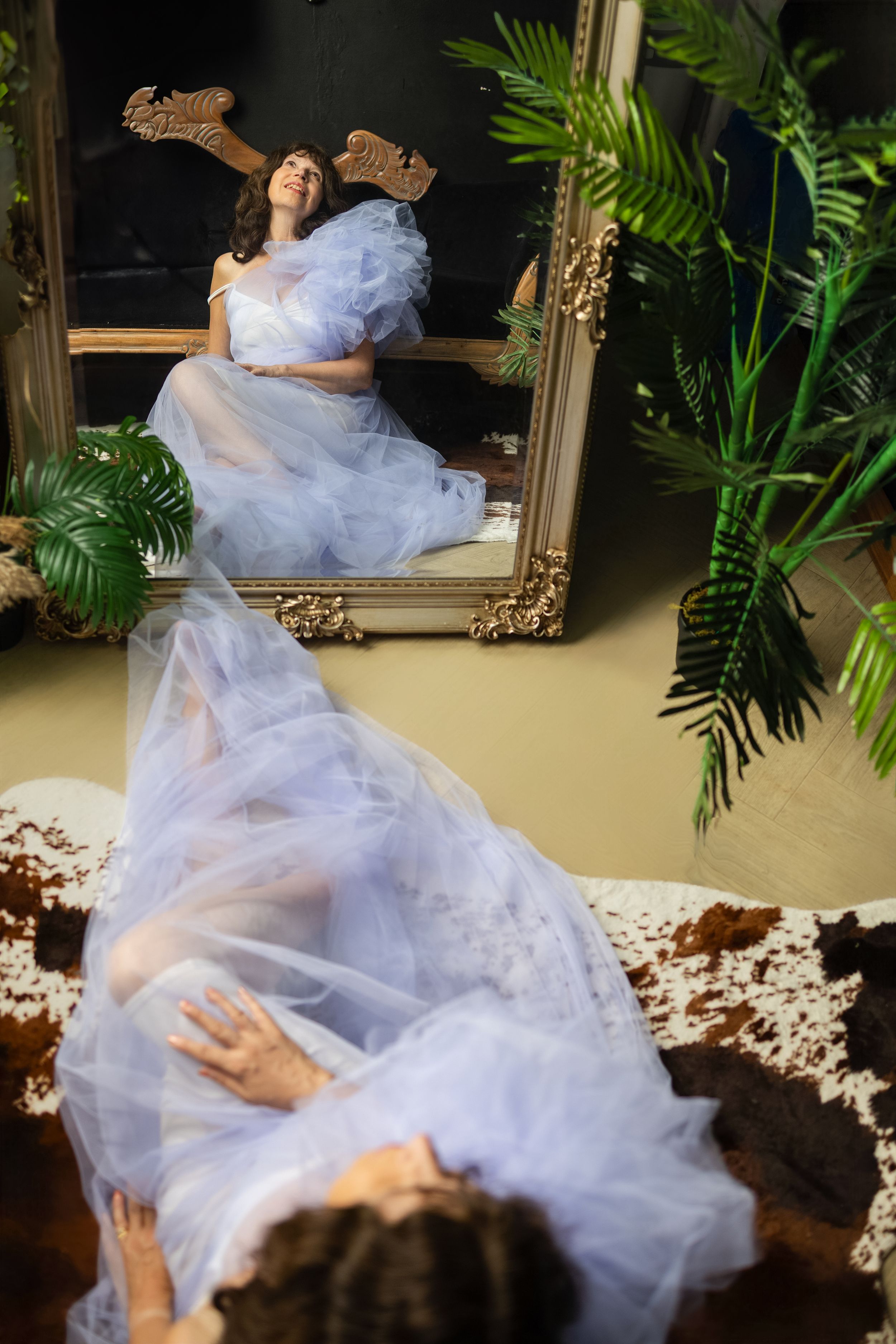 Dancer swirls in flowing light blue tulle dress against a tropical indoor setting with ornate mirror.