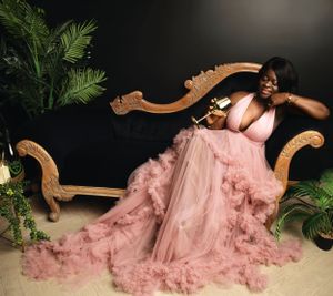 Elegant pink tulle gown flowing across antique chaise lounge with palm plants in dark studio setting.