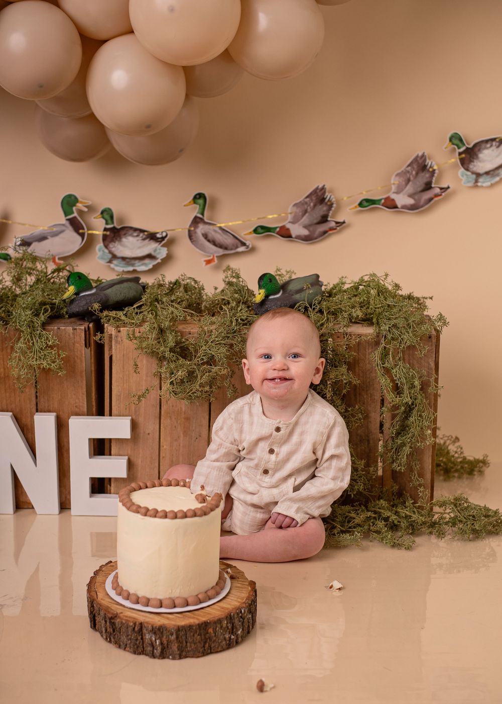 A rustic first birthday setup with wooden decor, balloons, and a simple white cake on a wood slice.