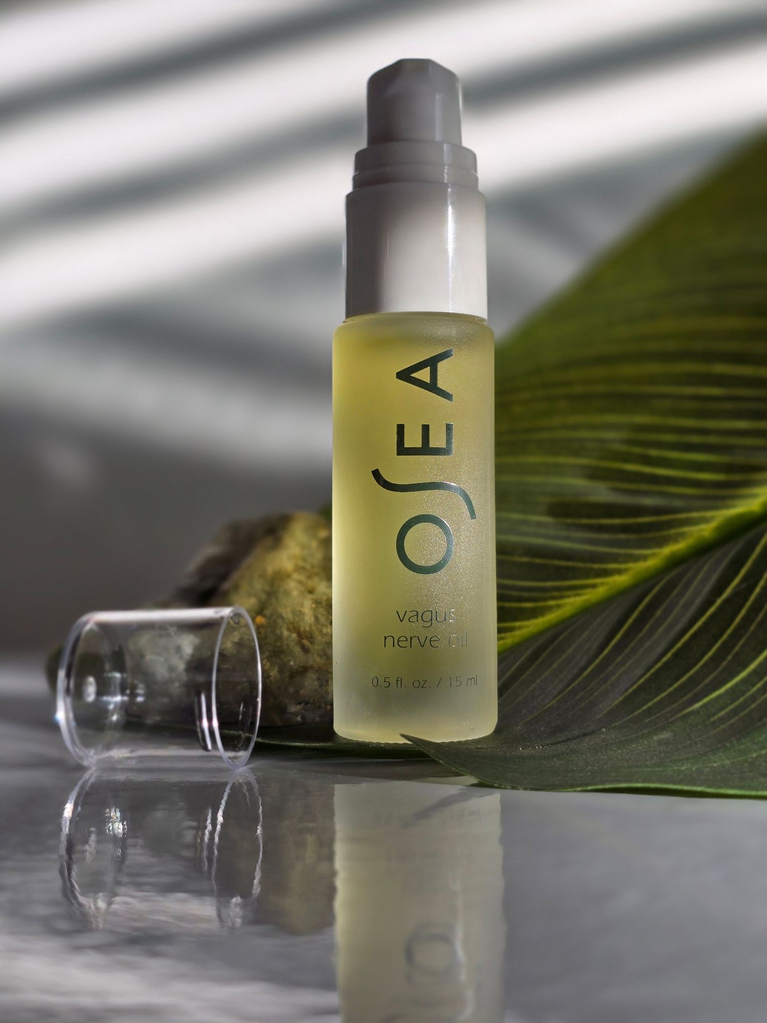 Bottle of premium OSEA skincare serum with yellow-tinted liquid displayed next to a tropical palm leaf on reflective surface.