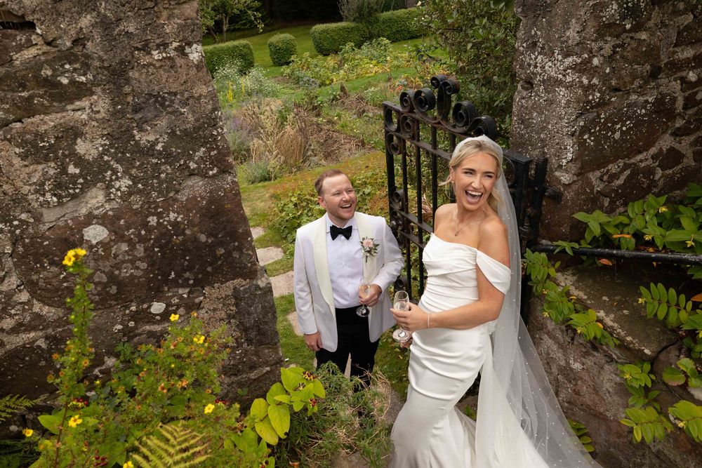 Wedding couple poses against stone wall backdrop in elegant formal attire.