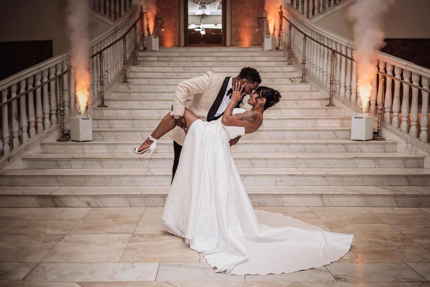 A romantic dip pose on an elegant marble staircase with warm lighting and a flowing white wedding gown.