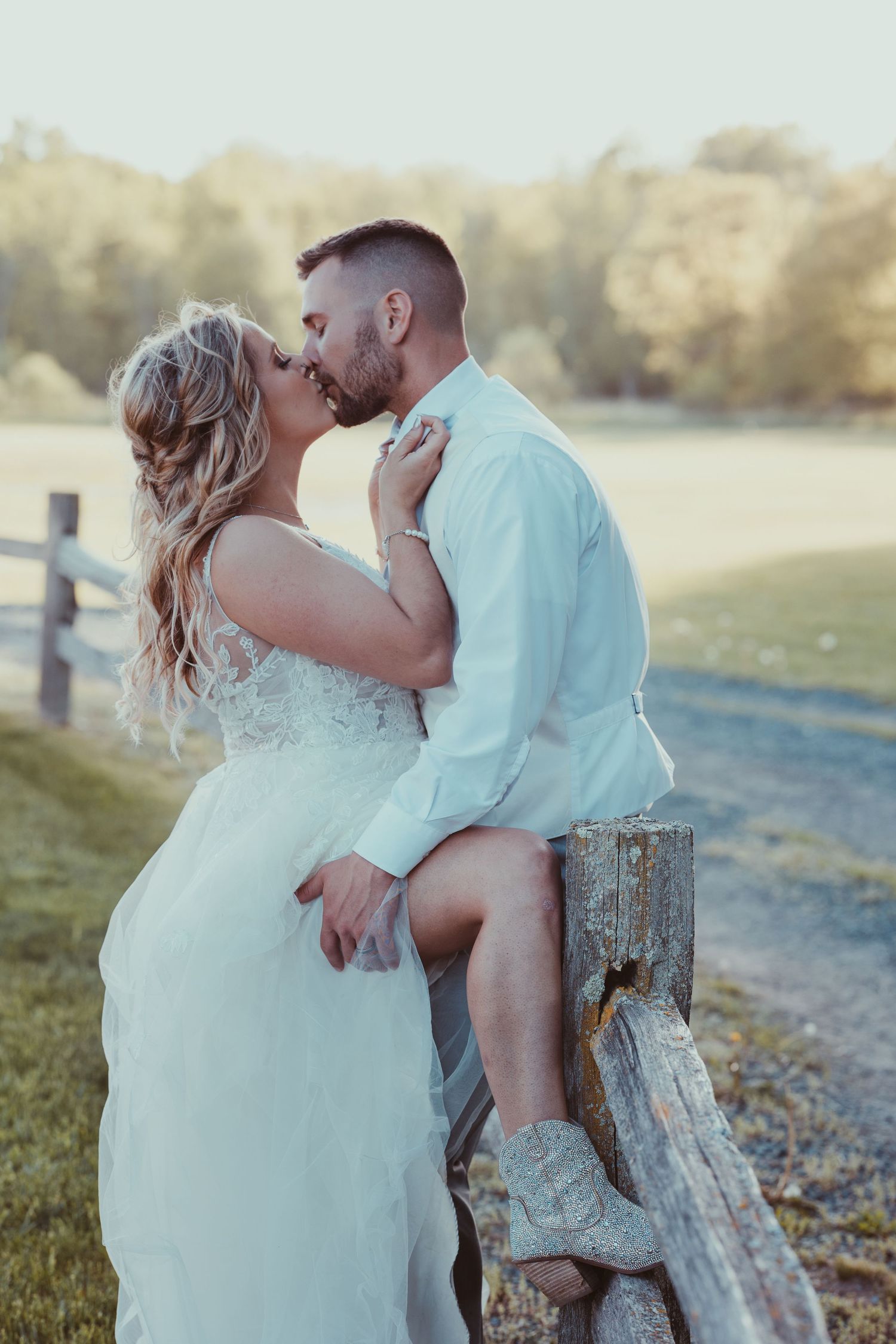 Romantic couple shares intimate moments while sitting on rustic wooden fence during golden hour photoshoot.