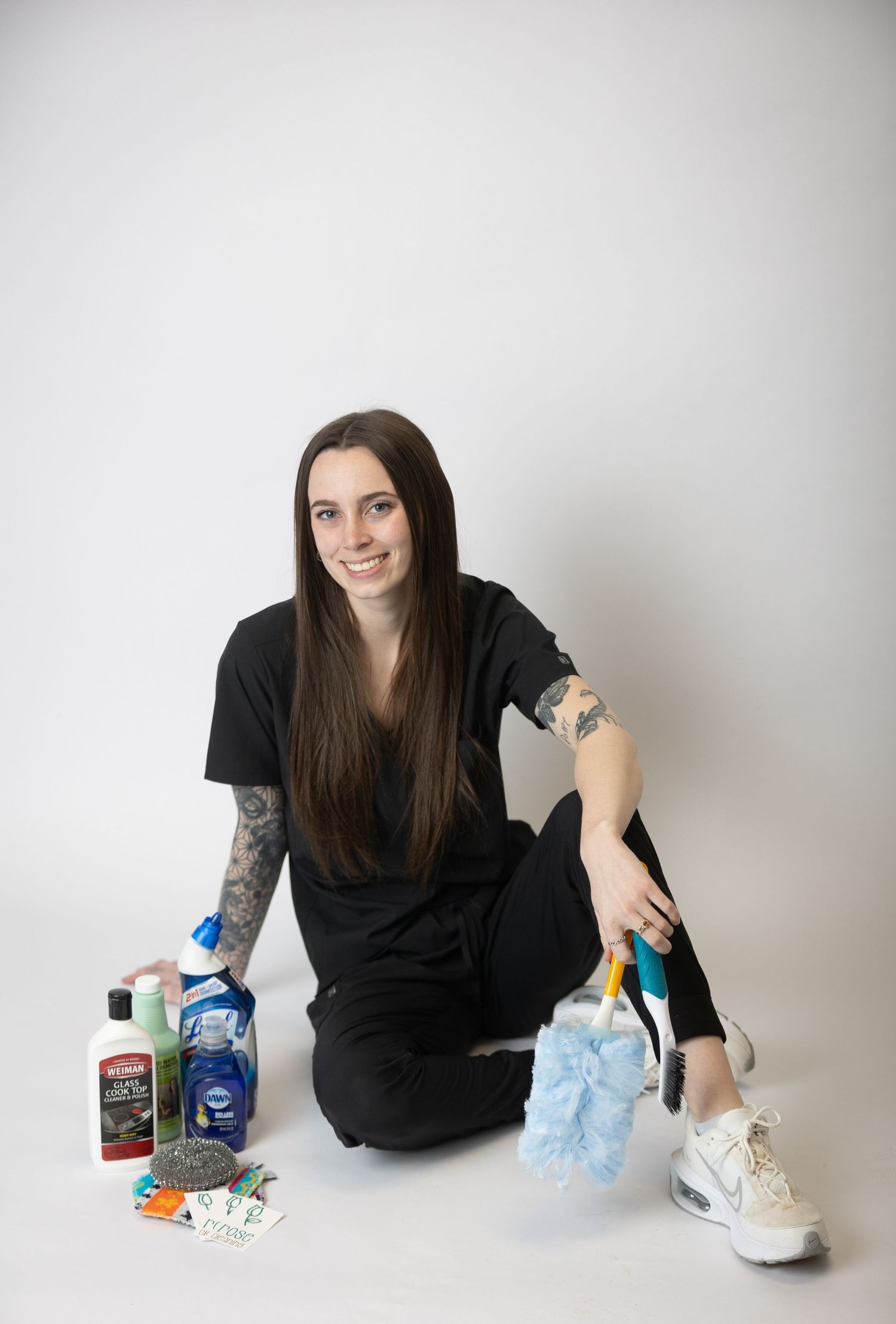 A person in black clothing sits on the floor with cleaning supplies and products.
