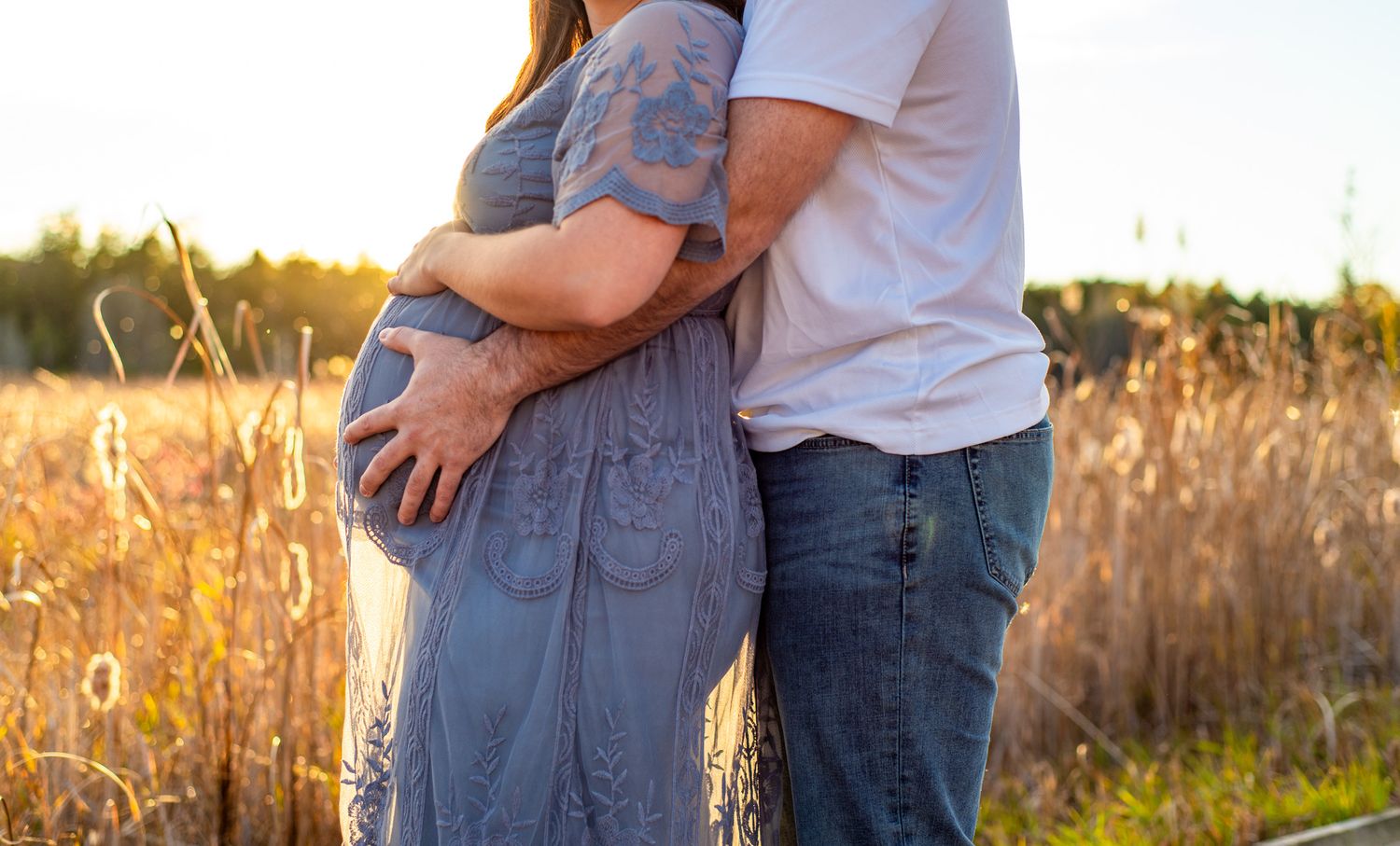 Two people embrace in a golden field at sunset with warm sunlight creating a romantic silhouette.