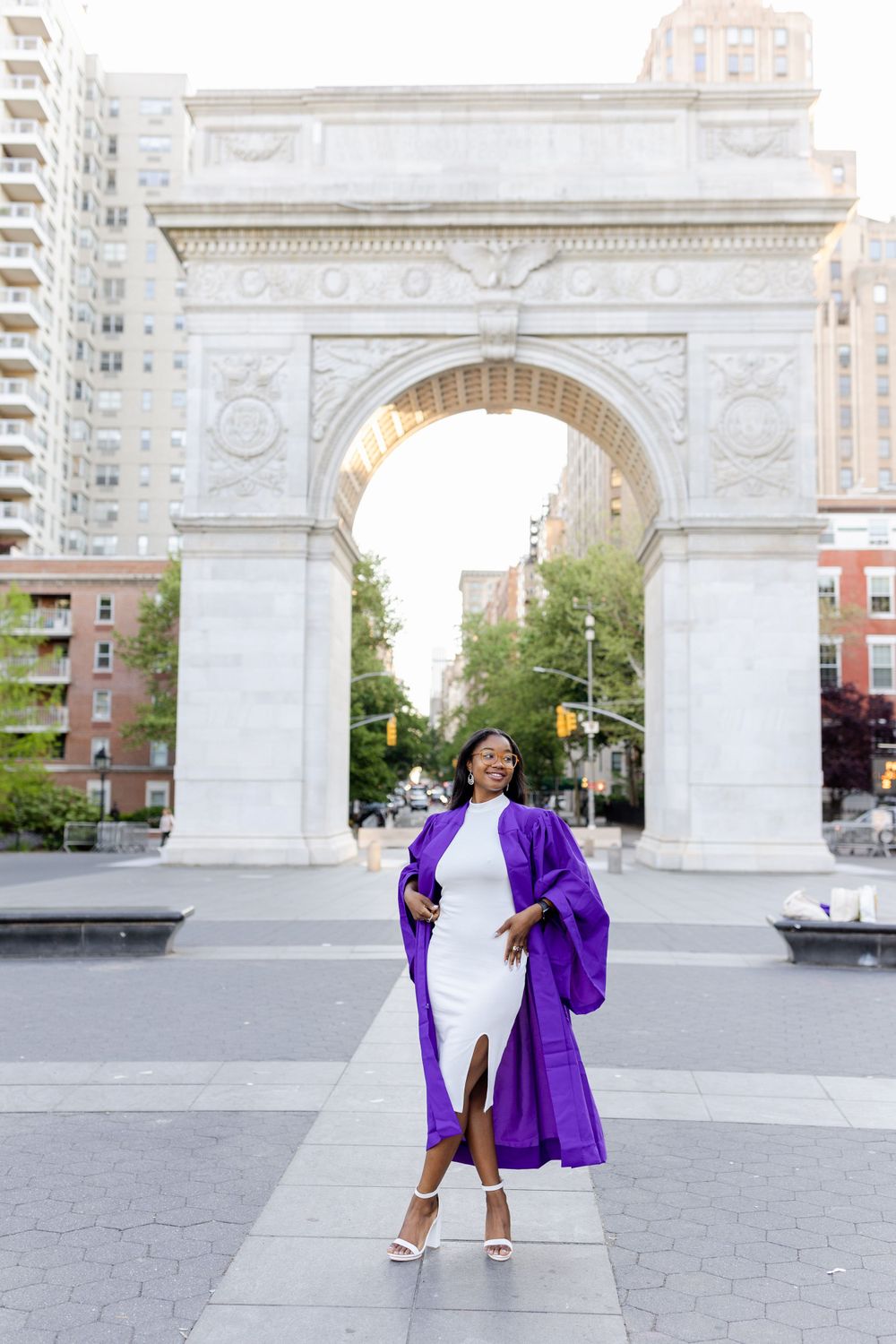 Graduate in flowing purple gown strikes elegant pose at Washington Square Park.