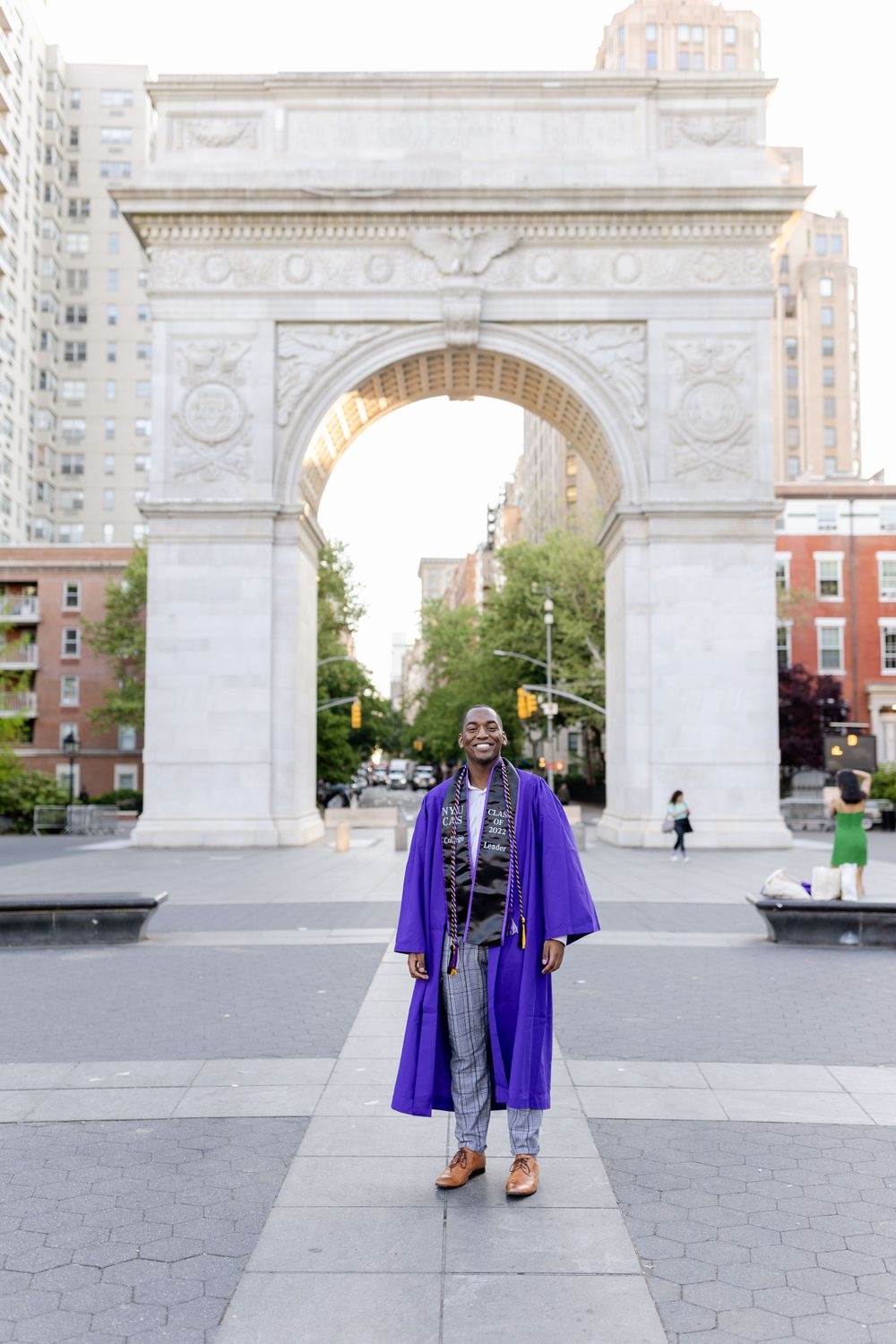 Graduate in purple commencement regalia poses confidently under Washington Square Arch.