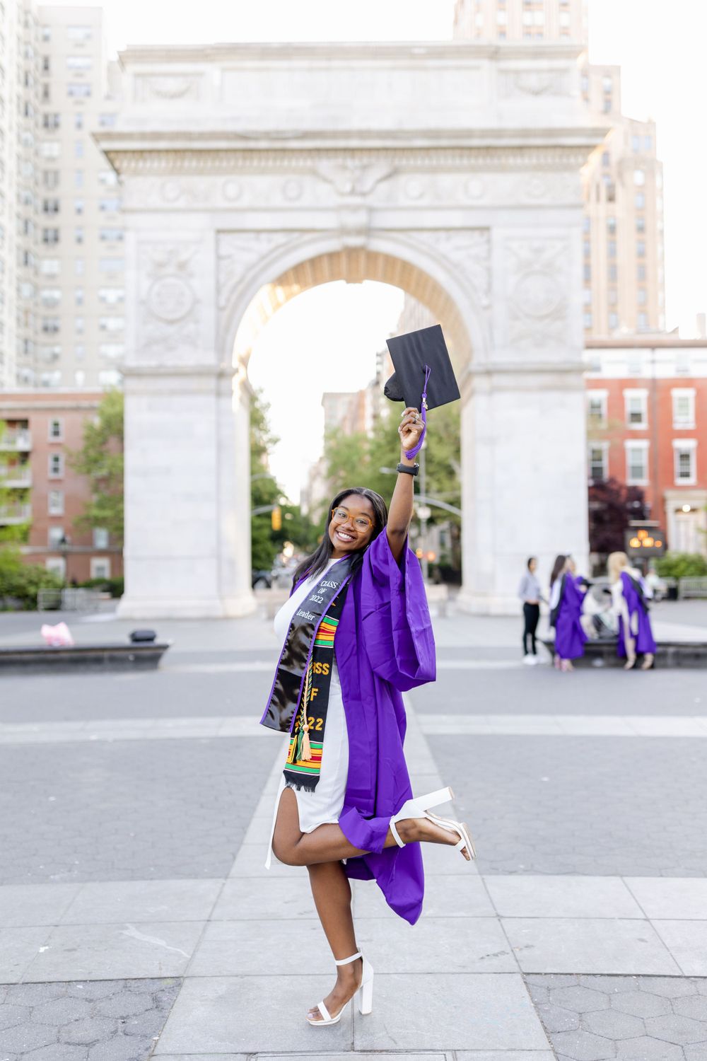 Excited graduate jumps for joy while holding diploma in front of iconic arch.