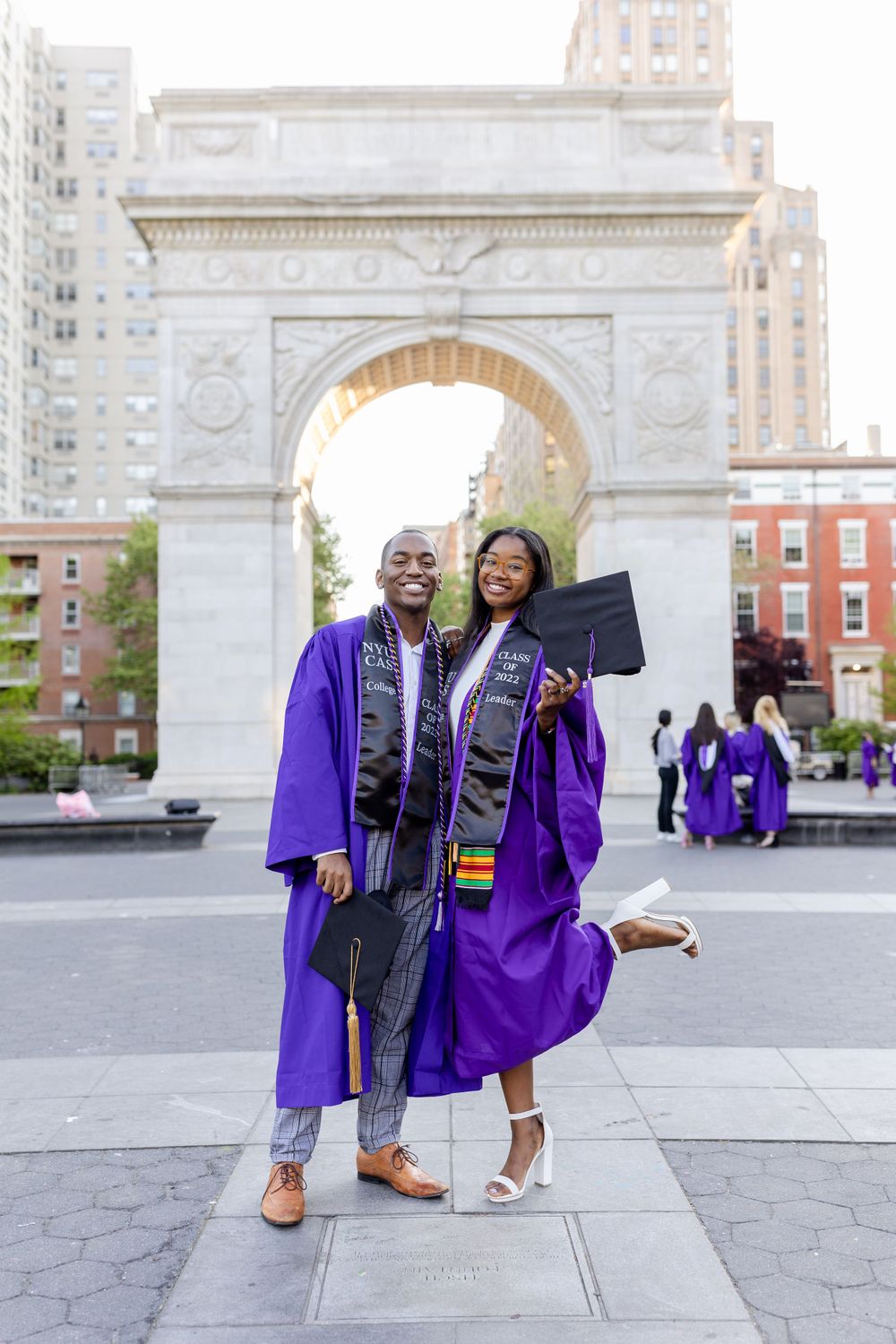 Graduates in purple commencement robes pose together in front of Washington Square Arch in NYC.
