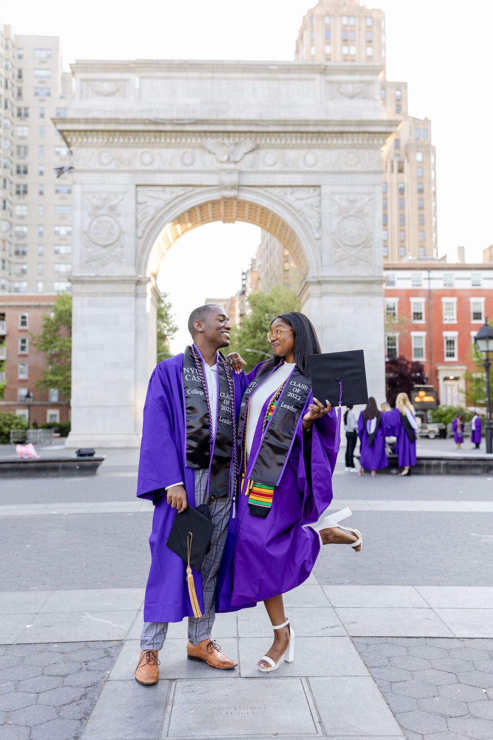 Graduates share a joyful moment in purple robes at Washington Square Park arch.