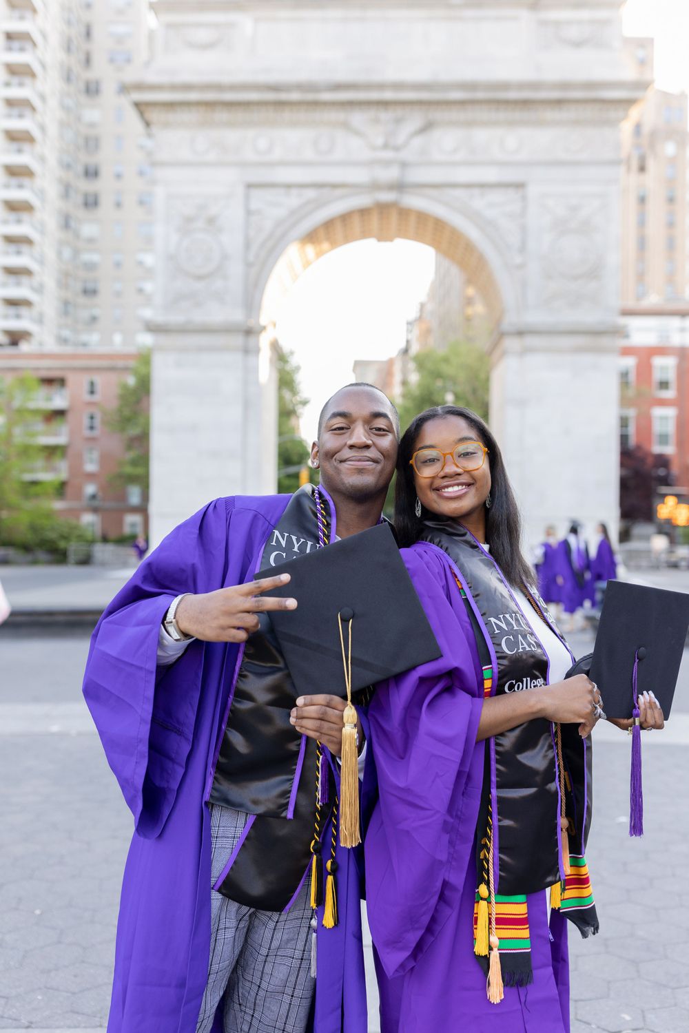 Graduates display their diplomas while wearing purple graduation gowns at Washington Square Park.