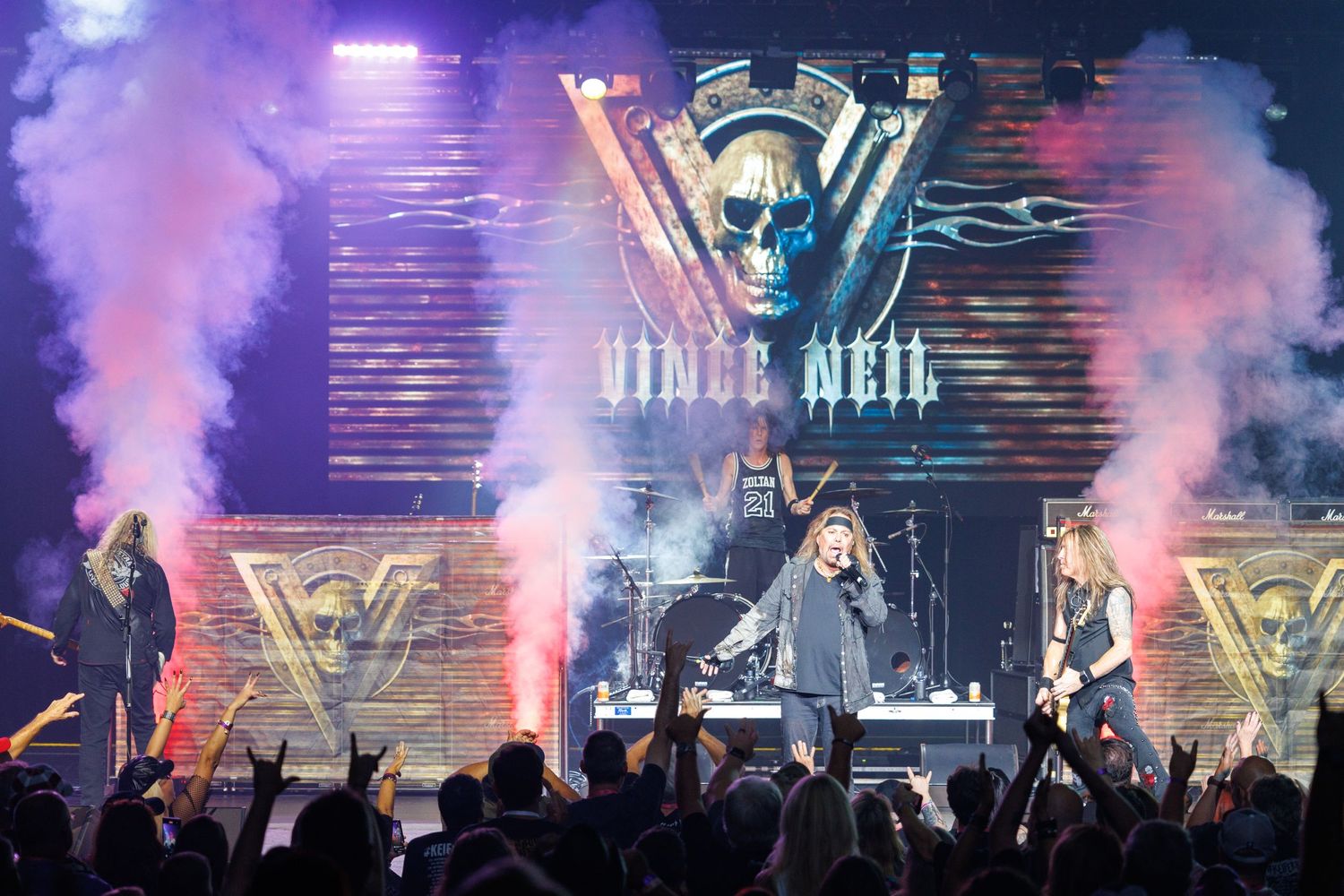 Rock band Vince Neil performs on stage with dramatic purple smoke and lighting effects during a live concert performance.