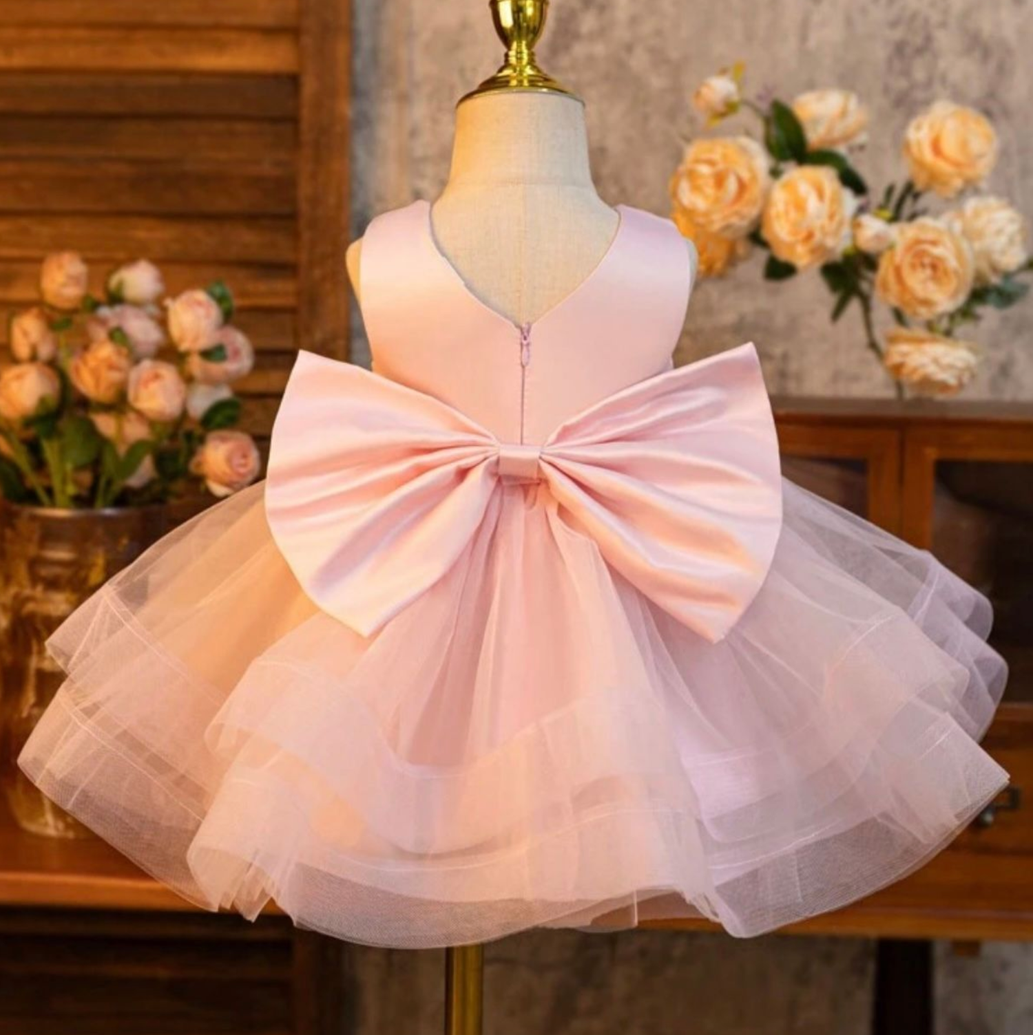 Pink tulle dress with large bow detail displayed against rustic background.