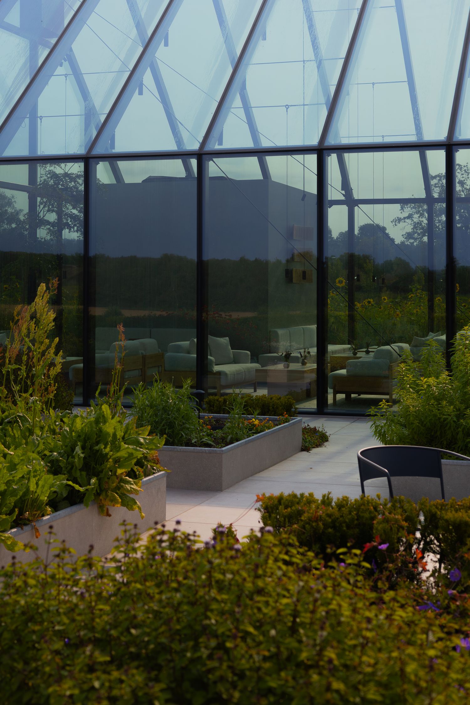 Glass-enclosed garden terrace with modern seating and raised planters features mountain views through transparent walls.