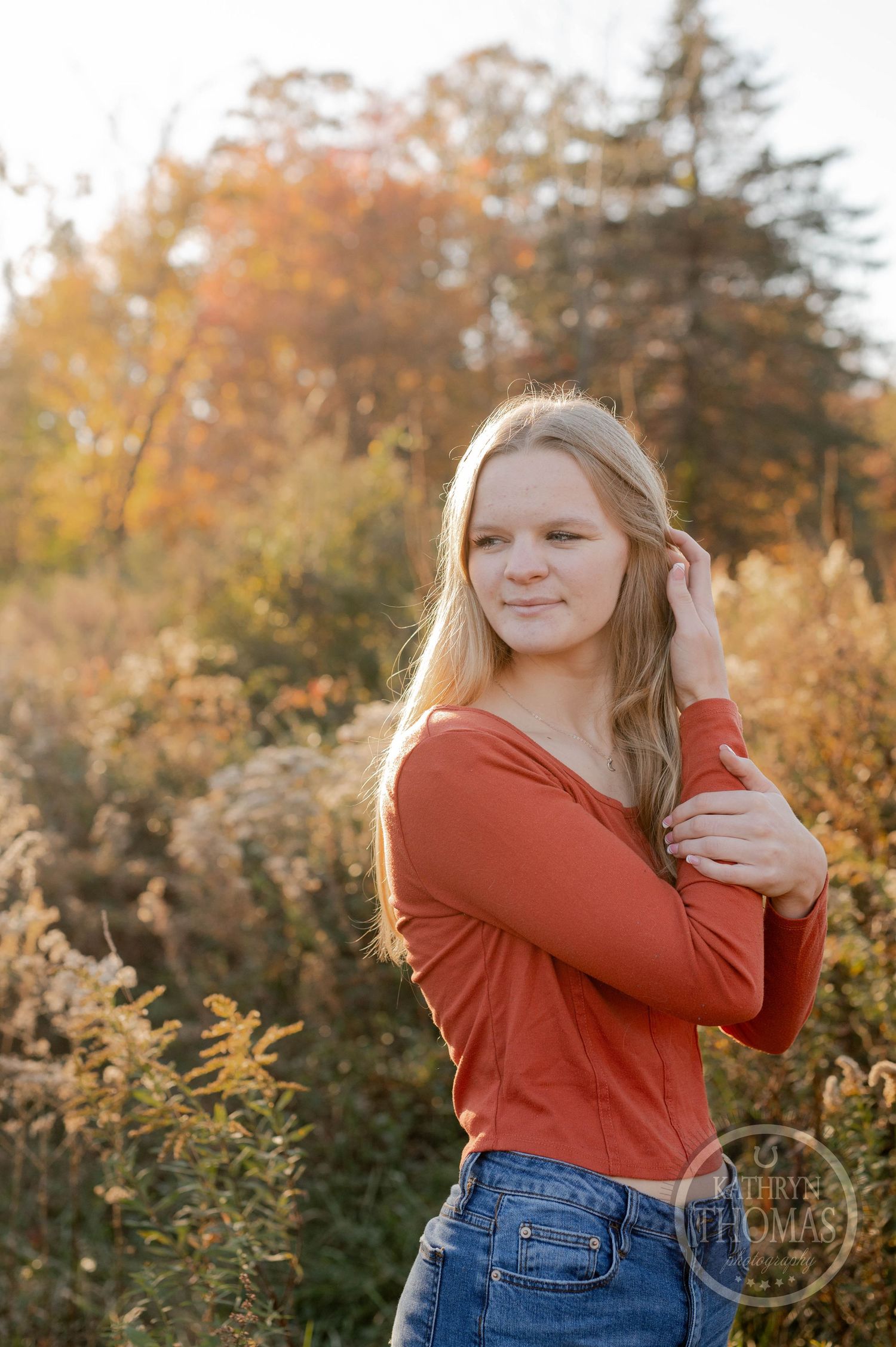Sunset portrait with warm lighting showing casual pose in front of fall foliage.