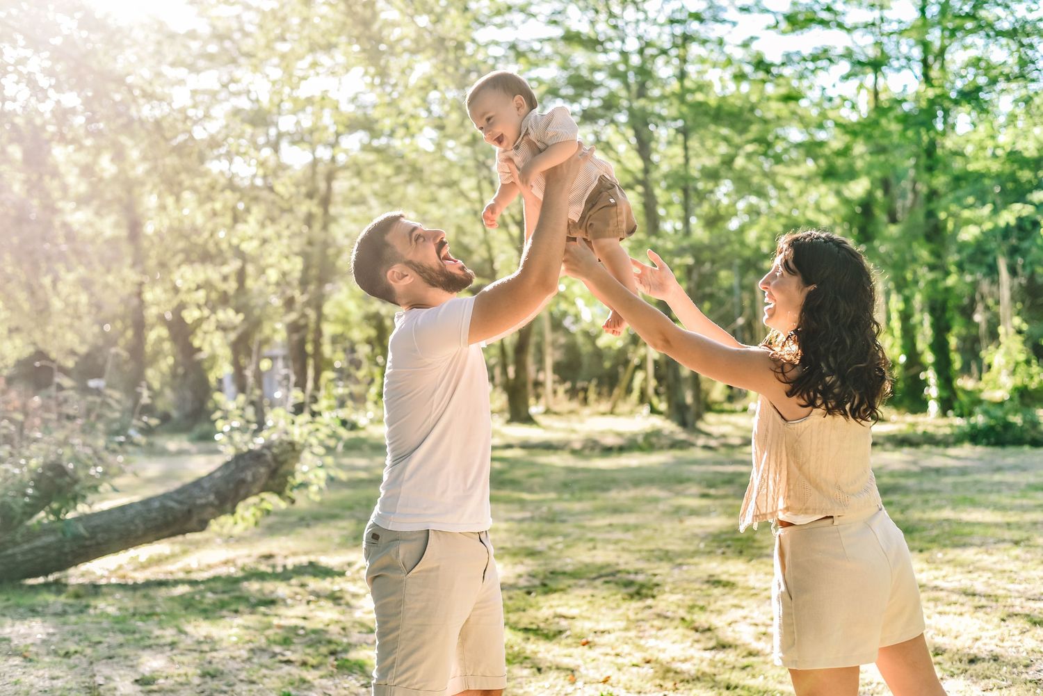 Family enjoying a playful moment lifting their child in a sunlit forest setting.