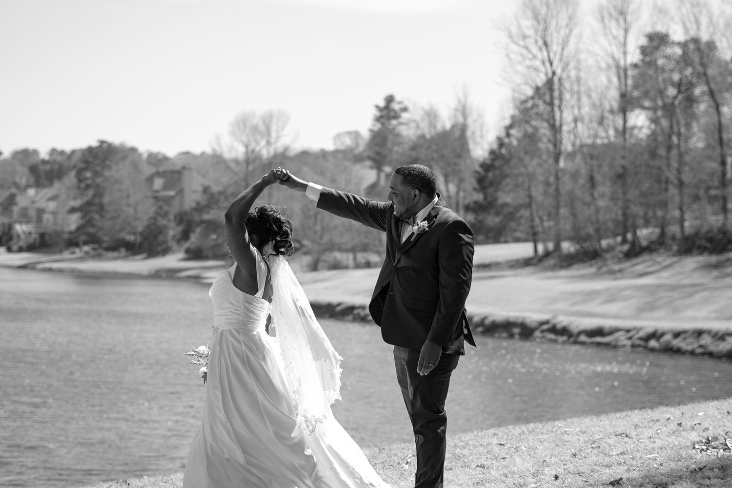Couple dancing outdoors by a lake in formal wedding attire.