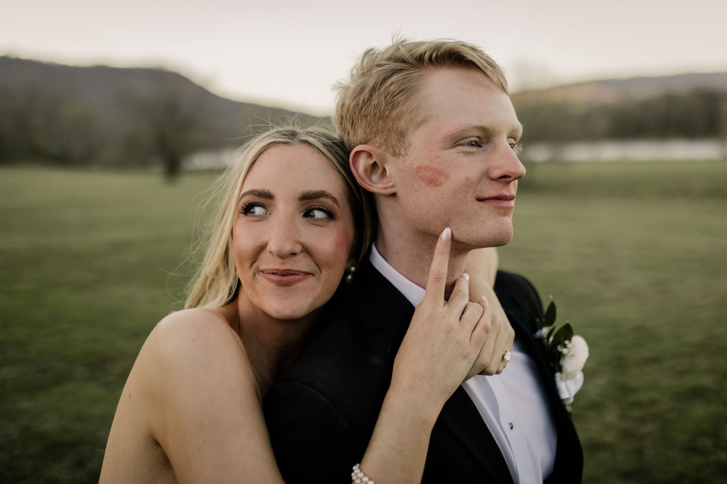 A close-up of a wedding couple embracing outdoors in a field at golden hour.