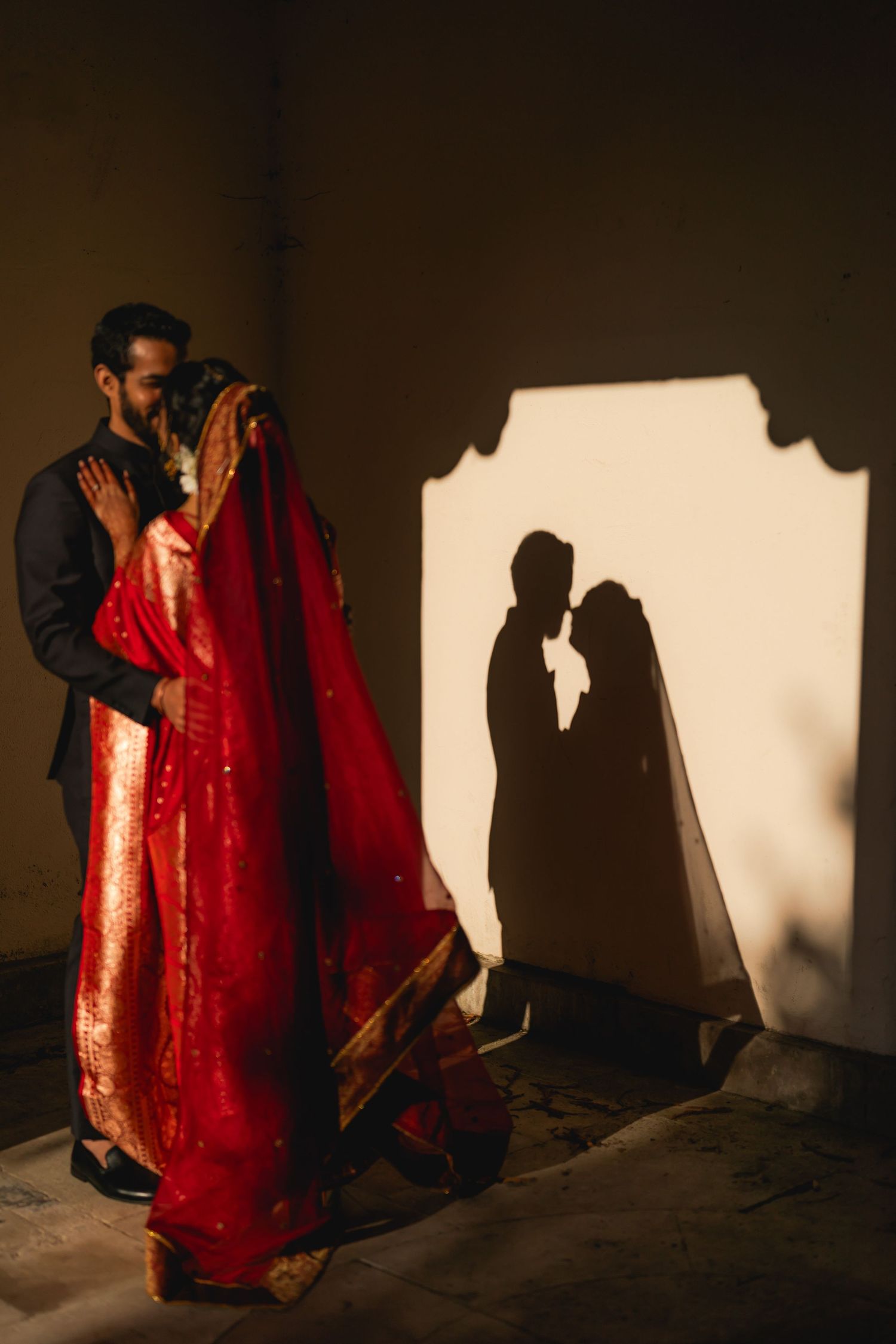 Indian couple walking together, bride in red saree and groom in black suit.