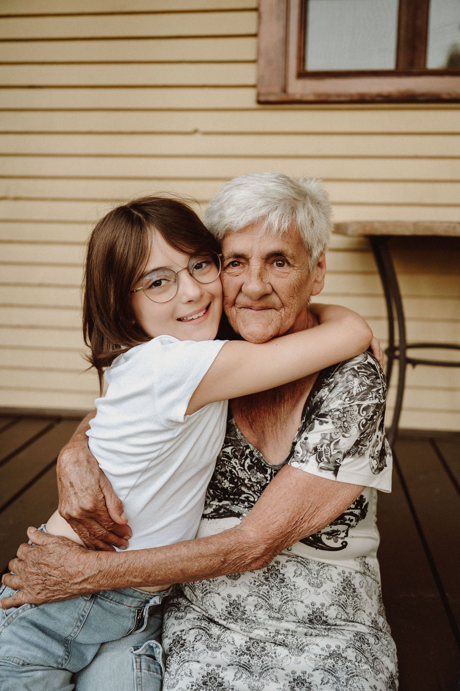 Heartwarming embrace between young person and elderly woman on wooden deck.